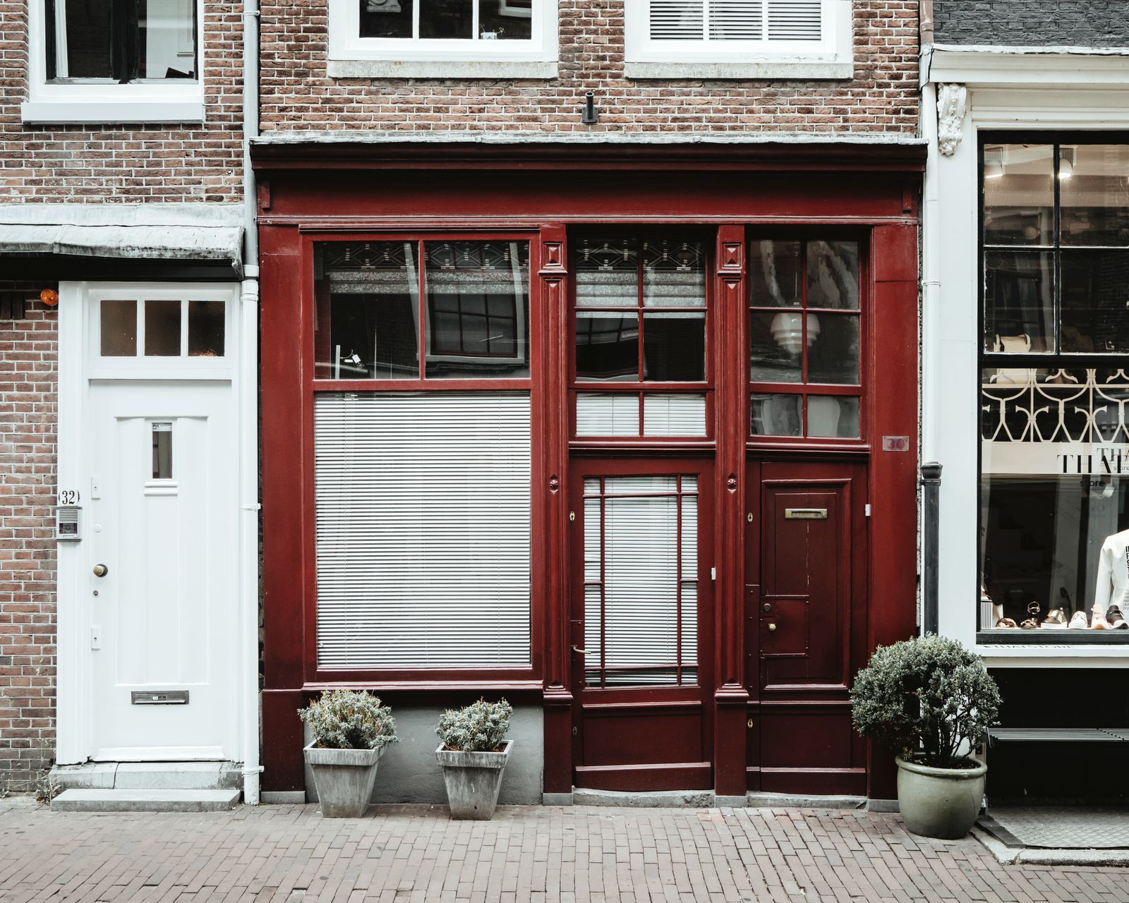 The brick front of the building, with a white door, red-framed windows and potted plants