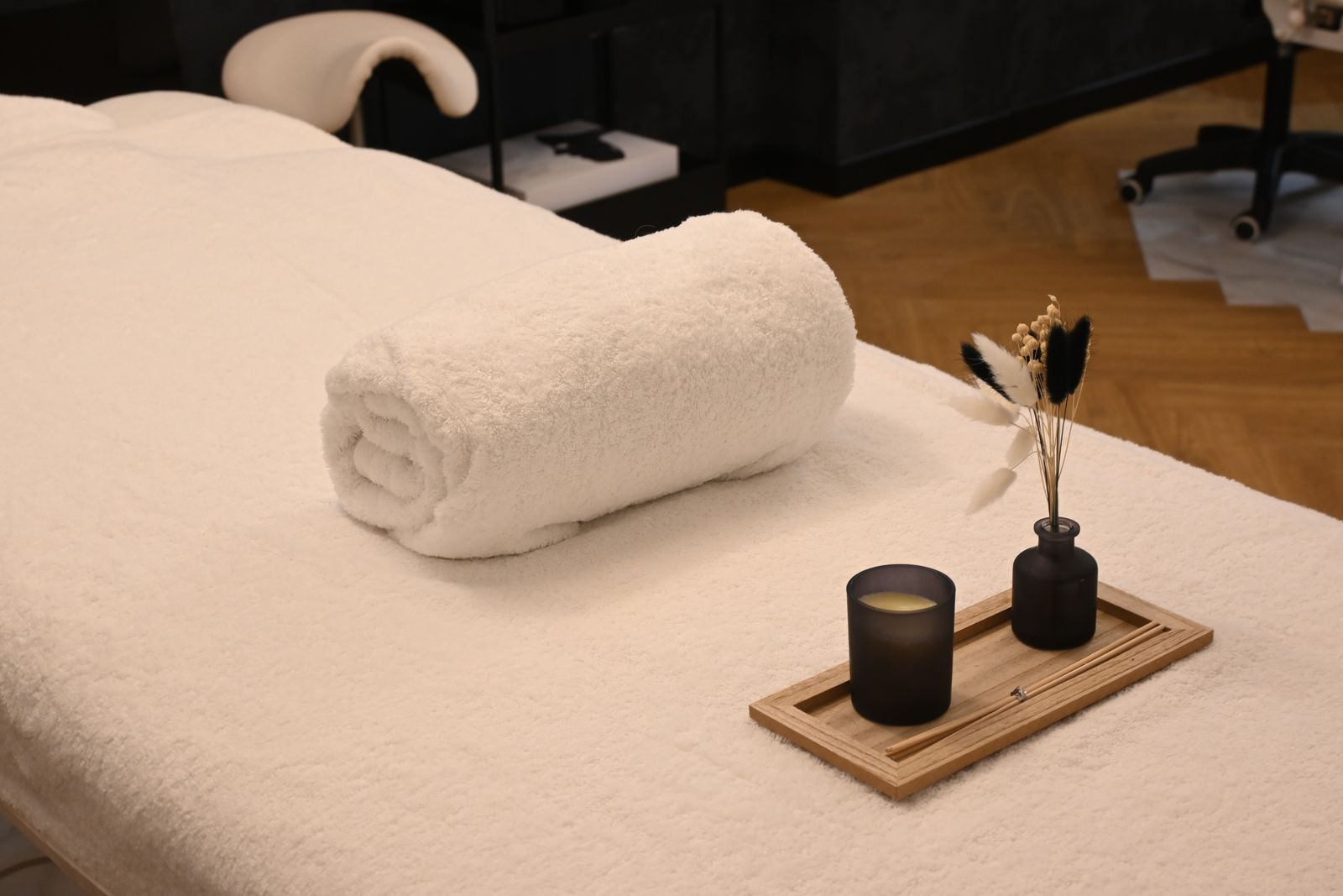 A massage table with a white sheet, a rolled towel and a small plant in a calm, softly lit room